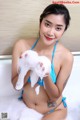 A woman in a blue bikini sitting in a bathtub with foam.