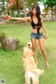 A woman in a black top and denim shorts playing with a dog.