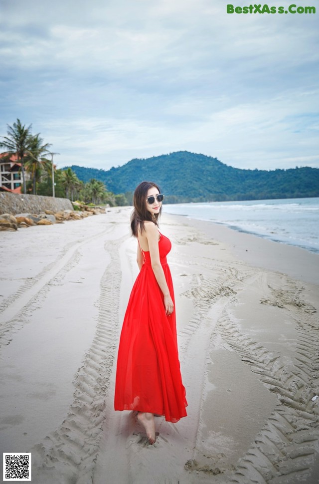 A woman in a red dress walking on the beach.