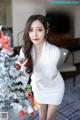 a woman in a white dress standing next to a christmas tree