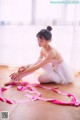 A young ballerina sitting on the floor tying up her ballet shoes.