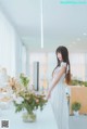 A woman in a white dress standing in front of a table with flowers.