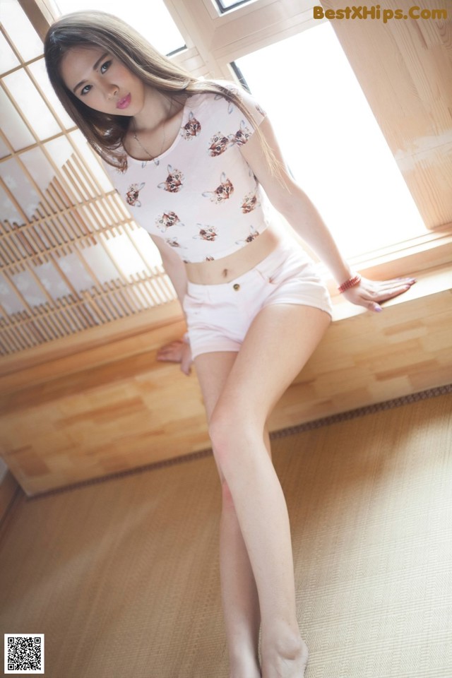 A woman in a white top and pink shorts posing for a picture.